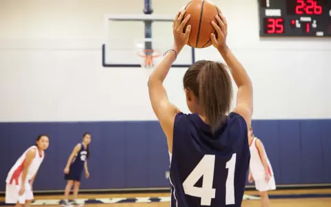 Ragazza con palla da basket, un ottimo sport per bambini iperattivi. In campo, altre giocatrici si preparano.