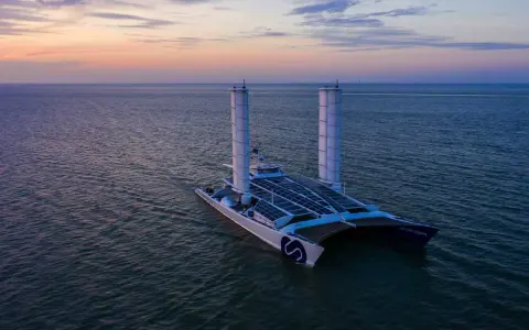 Der ENERGY OBSERVER, ein futuristisches Schiff mit Solarpaneelen und Windturbinen, gleitet bei Sonnenuntergang über das Meer.
