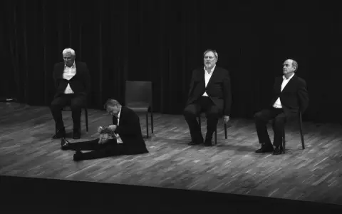 Czterech aktorów w garniturach na scenie. Jeden siedzi na podłodze, pozostali na krzesłach. Kwartet dla czterech aktorów.