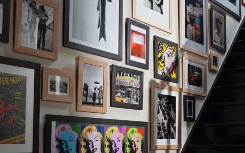 Un mur couvert de tableaux, dont des portraits de Marilyn Monroe, une scène de rue et une affiche de Spider-Man, le tout dans un cadre.