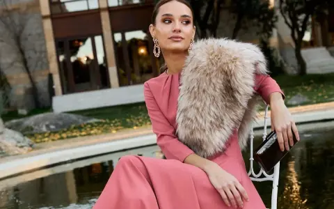 Elegante outfit fiesta invierno: vestido rosa palo, chal de pelo y bolso de mano.