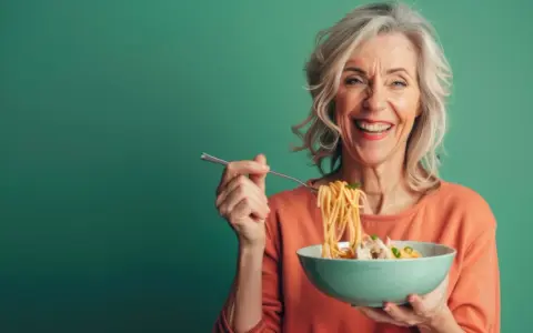 Uśmiechnięta seniorka zajada spaghetti. Pyszne danie, które pobudza co na apetyt dla seniora.