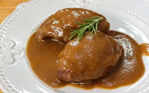 Deliciosas carrilleras de cerdo estofadas en salsa, coronadas con una ramita de romero fresco.