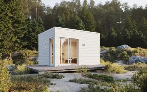 En vit, modern friggebod med stora fönster och altan, omgiven av skog och stenar. Perfekt för att bygga friggebod i naturen.