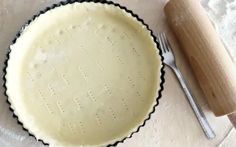 Surowe ciasto wegańskie w formie do tarty, obok wałek i widelec. Gotowe do pieczenia pysznego deseru.