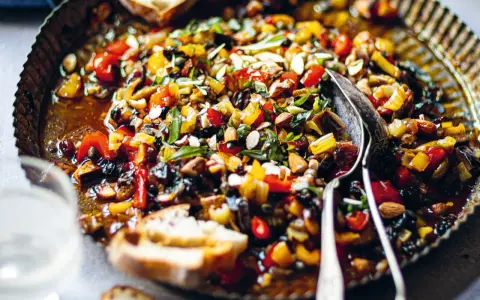 Pyszna caponata z selera z migdałami i oliwkami, podana w metalowej misie z pieczywem.