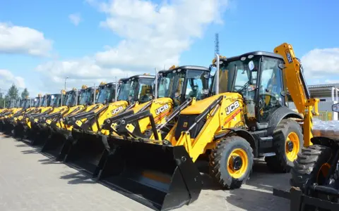 Rząd żółtych koparko-ładowarek JCB stoi na placu.
