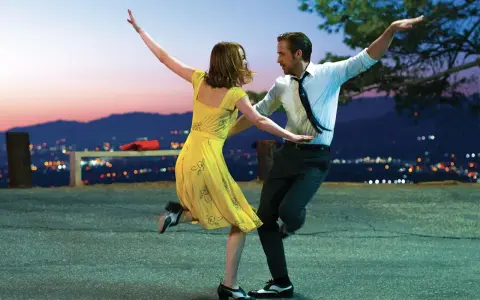 Coppia balla al tramonto, immersa nella musica diegetica che accompagna la loro danza, con la città illuminata sullo sfondo.