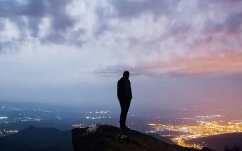 Silhouette di una persona su una rupe, con una città illuminata in lontananza. Un momento che fa amarcord, pensando a chi siamo e dove andiamo.