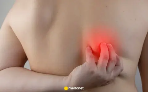 Osoba drapie się po plecach, gdzie widoczny jest czerwony obszar wskazujący na ból pod lewą łopatką.