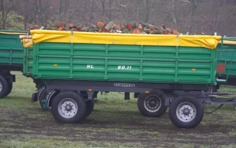 Zielona przyczepa Fortschritt HL 80.11 z drewnem pod żółtą plandeką.