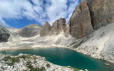 Il **lago di Antermoia**, incastonato tra imponenti vette rocciose, riflette il cielo azzurro e le nuvole bianche. Un gioiello alpino.
