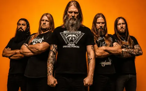 Amon Amarth tour: fem vikingar med långt hår och skägg poserar framför orange bakgrund.