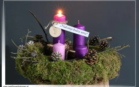 Wieniec adwentowy z zapaloną świecą, ozdobiony mchem, szyszkami i gałązkami. "Nadzieja budzi serce" - napis na pierwszej niedzieli adwentu.