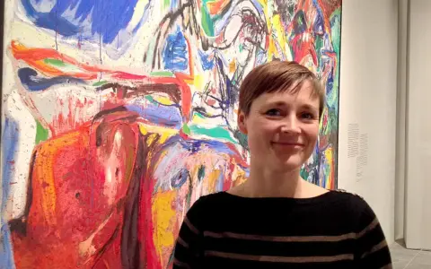 Kvinna ler framför en färgstark målning i Asger Jorns stil.