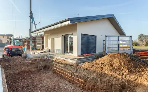Budowa domu 70m2. Wykop pod fundamenty, koparka i częściowo wykończony budynek.