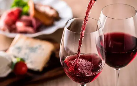 Vino tinto servido en copas, con tabla de quesos y embutidos al fondo. Una cata para apreciar la diferencia entre tempranillo y crianza.