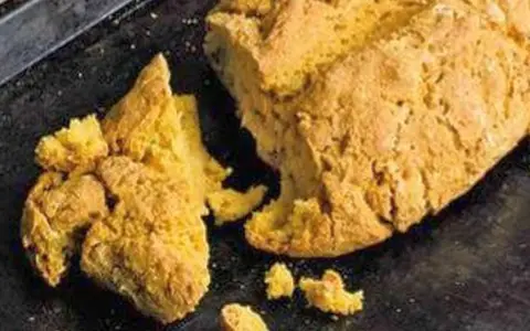 Goldgelbes, rustikales Brot, das nach Rezepten mit Lupinen aussieht, liegt auf einem dunklen Blech.