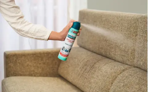 Mano rociando desinfectante en spray sobre un sillón de tela. Una forma fácil de saber como limpiar sillones de tela y eliminar olores.