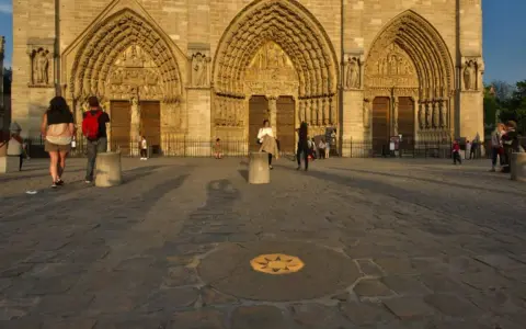 Devant Notre-Dame, le point zéro altitude marque le centre de Paris. Des visiteurs admirent la façade.