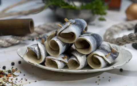 Gestapelte Rollmops Fisch auf einem Teller, garniert mit Gewürzen und Holzspießen.