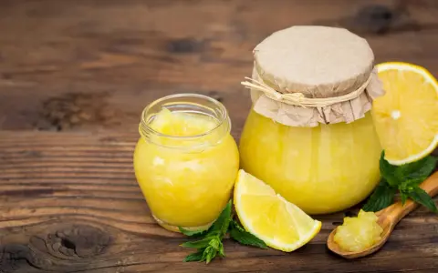 Due vasetti di marmellata di limoni, limoni freschi e foglie di menta su un tavolo di legno.
