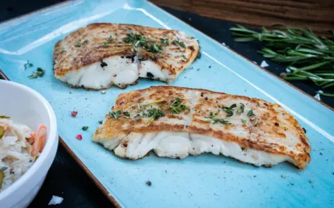 Zwei perfekt gegrillte Kabeljaufilets, mit Kräutern bestreut, serviert auf einem blauen Teller. Genießen Sie kabeljau grillen ohne alufolie!
