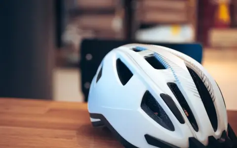 Biały kask rowerowy na drewnianym stole. Pamiętaj o bezpieczeństwie, bo jazda bez kasku to mandat.