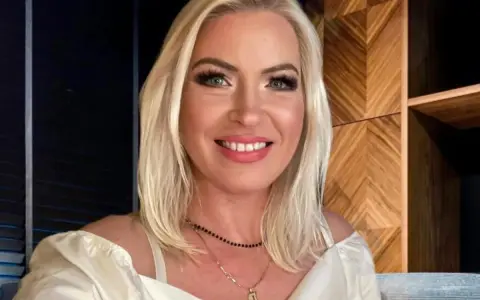 Uśmiechnięta Joanna Janikowska-Samojłowicz w białej bluzce z odkrytymi ramionami, z naszyjnikami na szyi.