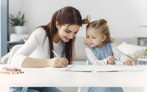Mama uczy córkę odejmowania do 10. Dziewczynki piszą w zeszytach, a obok leżą kolorowe flamastry.