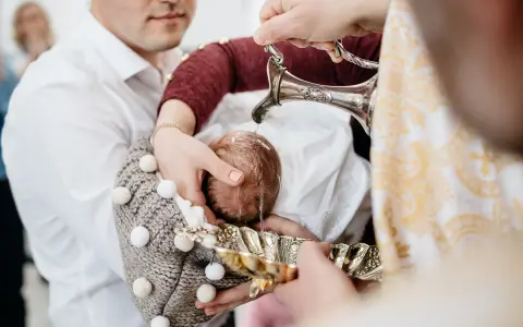 Woda święcona spływa na główkę dziecka podczas ceremonii na chrzcie.