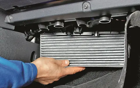Wymiana filtra kabinowego Passat B7: ręka wyciąga zużyty filtr z obudowy pod schowkiem.