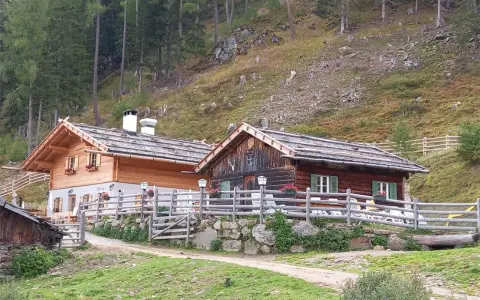 Tablander Alm a Parcines, con due baite in legno e recinzione, immerse nel verde di un pendio boscoso.