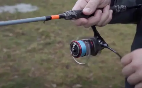 Daiwa Fuego Camo Spin Test: Eine Hand hält eine Angelrute mit Camo-Griff und einer Rolle mit blauer Schnur.
