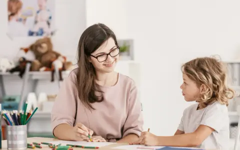 Bambina con ADHD, durante una sessione di diagnosi, disegna con una maestra sorridente.