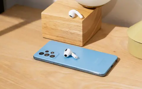 AirPods liegen auf einem blauen Samsung-Smartphone und einem Holzblock.