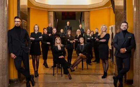 Grupa profesjonalistów w czarnych strojach pozuje w eleganckim wnętrzu.