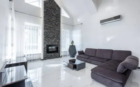 Un moderno salón con un sofá gris oscuro, chimenea de piedra y suelo de mármol blanco.