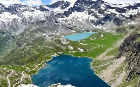Laghi alpini blu e turchese ai piedi del Colle del Nivolet, con strade tortuose e montagne innevate sullo sfondo.
