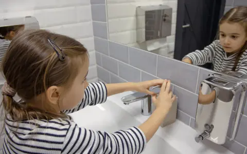Niña se lava las manos en el baño, un gesto importante para la higiene y la prevención del toc en niños.