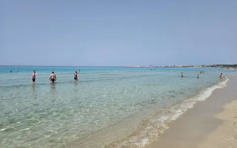 Persone in piedi nell'acqua cristallina, con la costa di Gallipoli sullo sfondo. Un perfetto giorno di mare.
