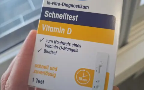 Hand hält eine Verpackung für einen Vitamin-D-Schnelltest mit einem Bluttest-Streifen.