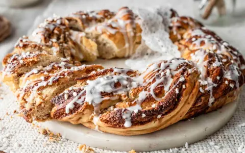 Ein goldbrauner nusskranz hefe, mit Zuckerguss und Perlen verziert, liegt auf einem Marmorsockel.
