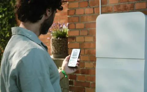 Man kollar sin mobil som visar information om sin batteribank hemma.