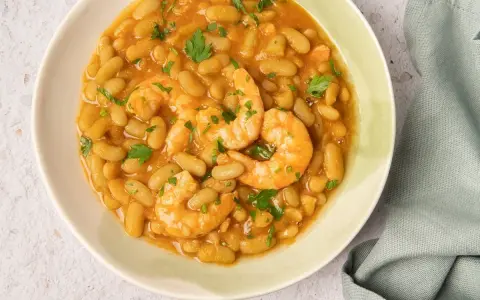Plato de verdinas con langostinos, un guiso reconfortante y sabroso, decorado con perejil fresco.