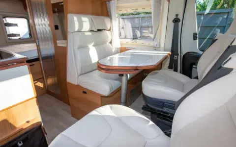 Interno camper con sedili e divanetti in ecopelle o similpelle bianca, tavolo e finiture in legno.