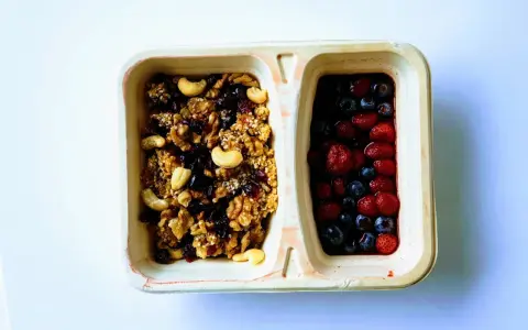 Dwie przegródki pojemnika: jedna z granolą i orzechami, druga z jagodami i truskawkami. Czy kasza jaglana ma gluten? Ta granola wygląda na bezglutenową!