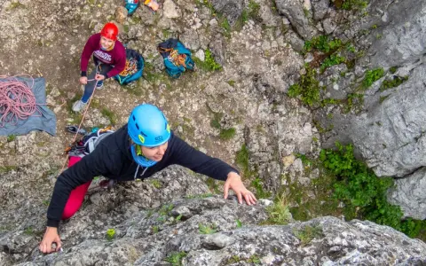 Uczestniczka kursu wspinaczkowego wspina się po skale, asekuruje ją koleżanka.