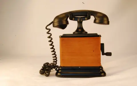 Stary telefon na korbkę z drewnianą obudową i czarną słuchawką.