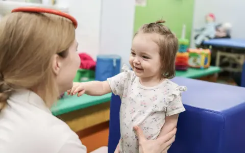 Uśmiechnięte dziecko wyciąga rączkę do terapeuty. To przykład, co to jest integracja sensoryczna – wspieranie rozwoju dziecka.